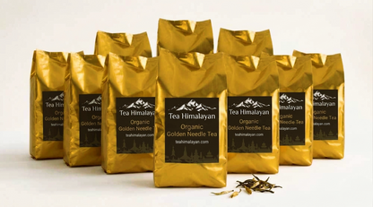 Nine shiny gold tea bags arranged in a fan shape on a white background, with a small pile of loose tea leaves in front. Each bag has a black label reading 'Tea Himalayan Organic Golden Needle Tea'.