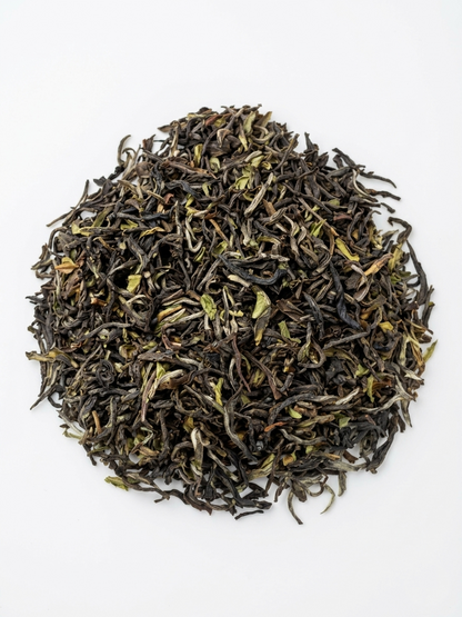 A pile of loose-leaf tea leaves, showing dark brown and black dried buds with light green and silver-white tips, arranged in a circular mound on a plain white background.