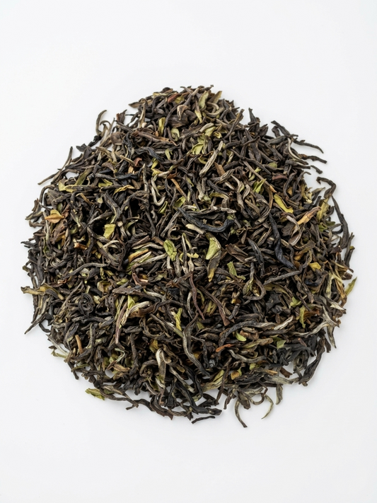 A pile of loose-leaf tea leaves, showing dark brown and black dried buds with light green and silver-white tips, arranged in a circular mound on a plain white background.