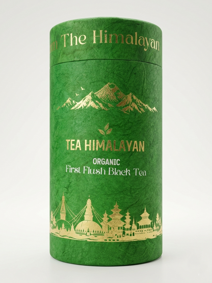 A cylindrical green tea tin with gold foil illustrations of mountains and buildings, labeled 'The Himalayan' and 'TEA HIMALAYAN ORGANIC First Flush Black Tea', on a light gray background.