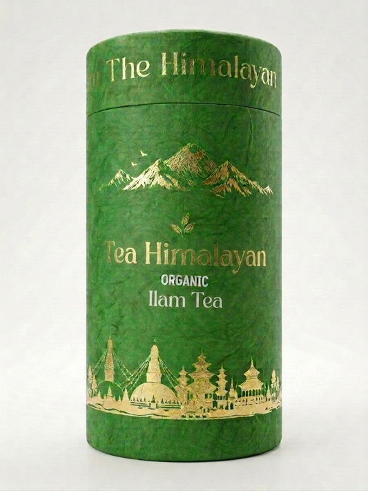 A green cylindrical tin canister of Tea Himolayan Organic Ilam Tea, featuring gold foil illustrations of the Himalayan mountains and traditional architecture, set against a plain white background.