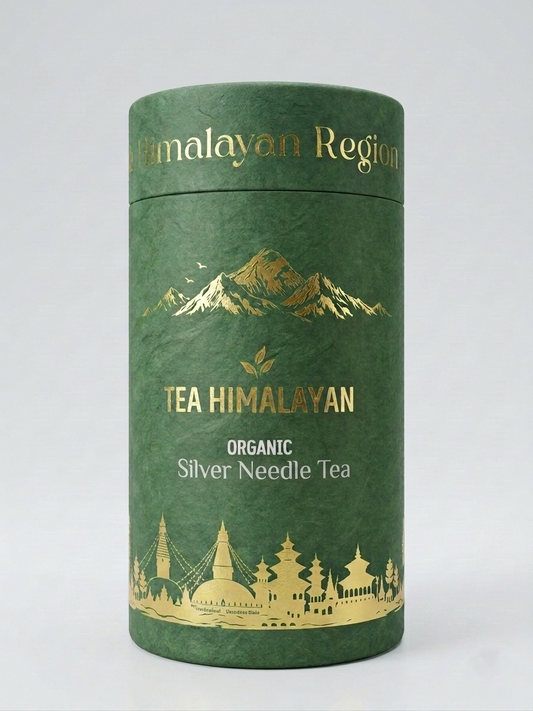 A cylindrical green tea tin with gold foil text reading 'TEA HIMALAYAN' and 'ORGANIC Silver Needle Tea', plus mountain and temple illustrations, photographed on a light gray background.