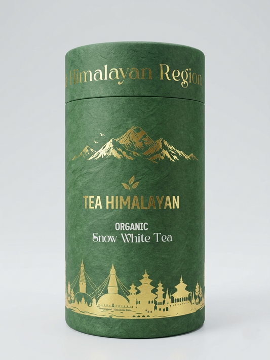 A cylindrical green tea canister with gold foil text reading 'TEA HIMALAYAN' and 'ORGANIC Snow White Tea', plus mountain and architectural illustrations, photographed on a light gray studio background.